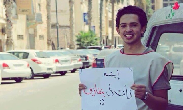 Tawfiq Bin Saud holds a sign that reads 'smile you are in Benghazi' (Photo: Social Media)