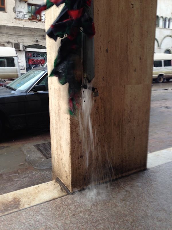 Water gushes down a drainpipe adorned with Libyan flags in Tripoli Old Town